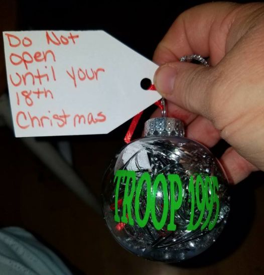 a hand holding a christmas ornament with the word troop on it and a tag that says do not open until your 10th christmas