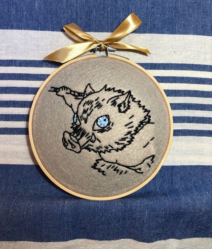 an embroidered cat ornament hanging on a blue and white striped cloth with gold ribbon