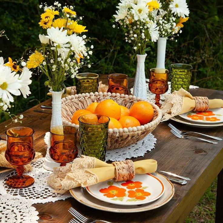 the table is set with oranges and flowers in vases, plates, napkins and glasses