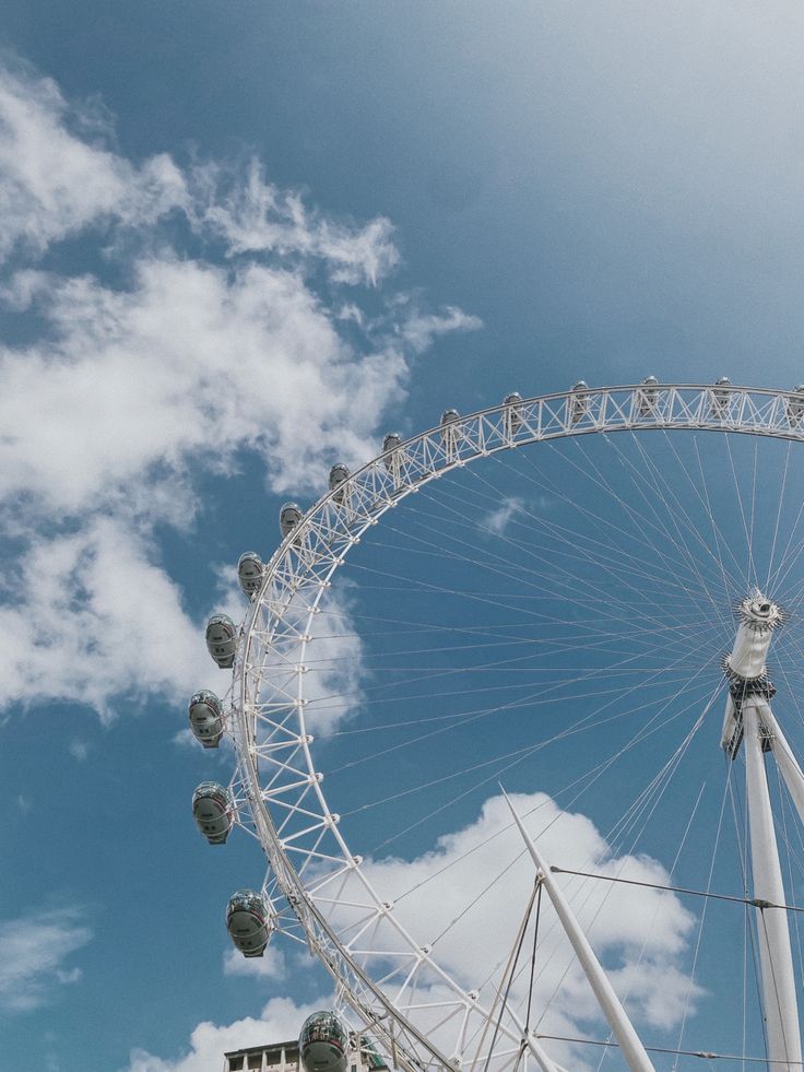 a large ferris wheel sitting next to a tall building under a blue sky with clouds