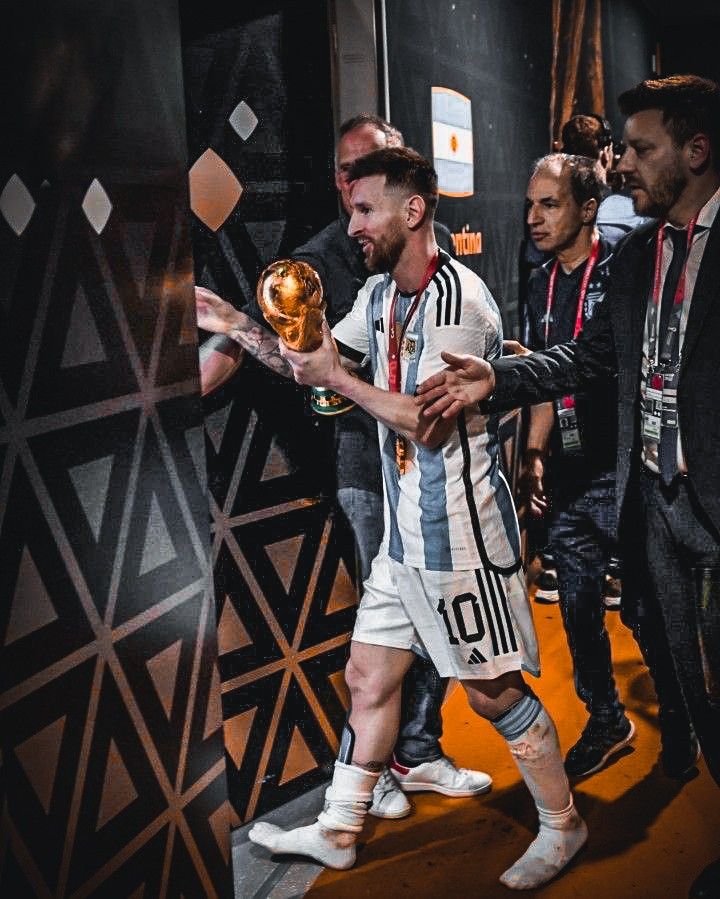 a man holding a soccer ball in his right hand while walking past other men wearing suits and ties