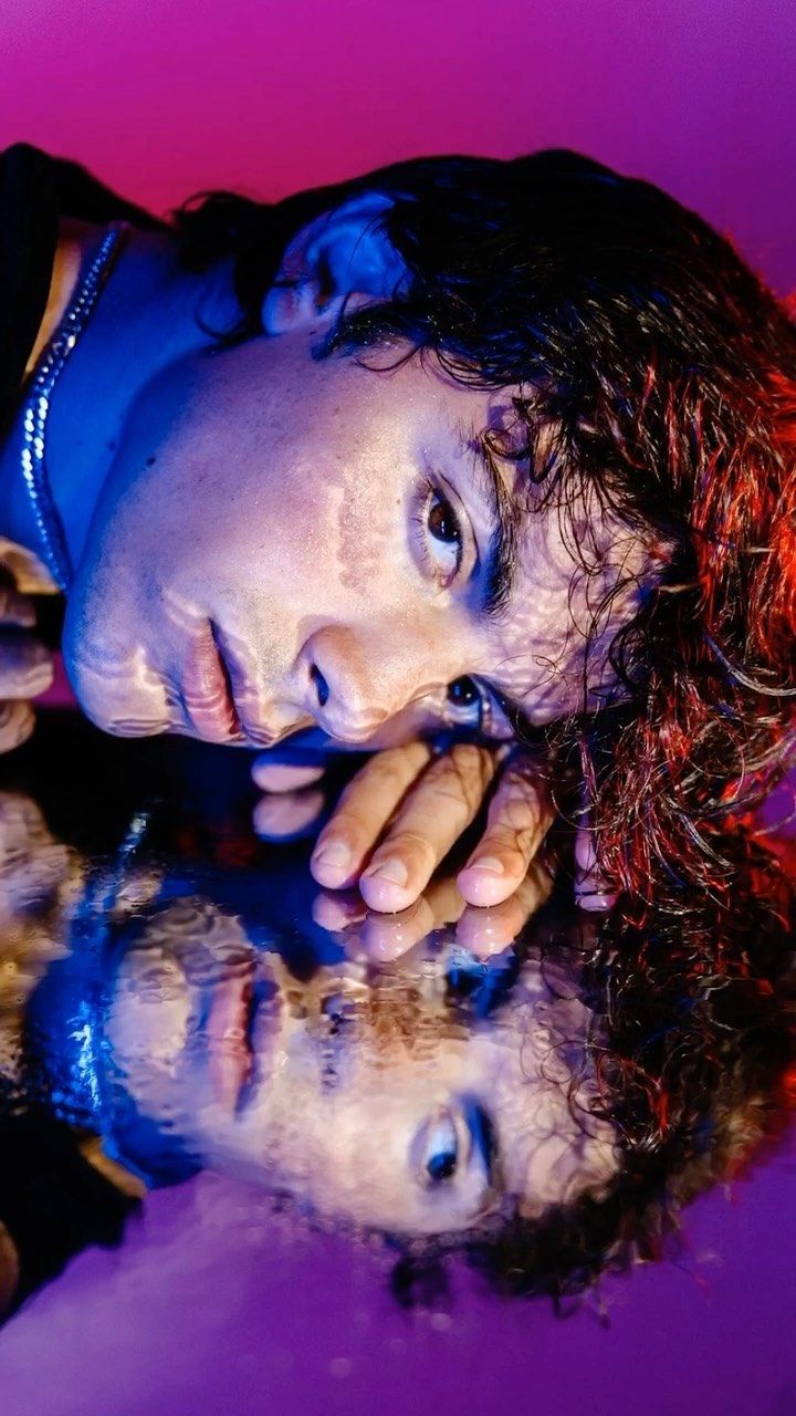 a man laying on top of a table next to a purple and pink wall with his reflection in the water