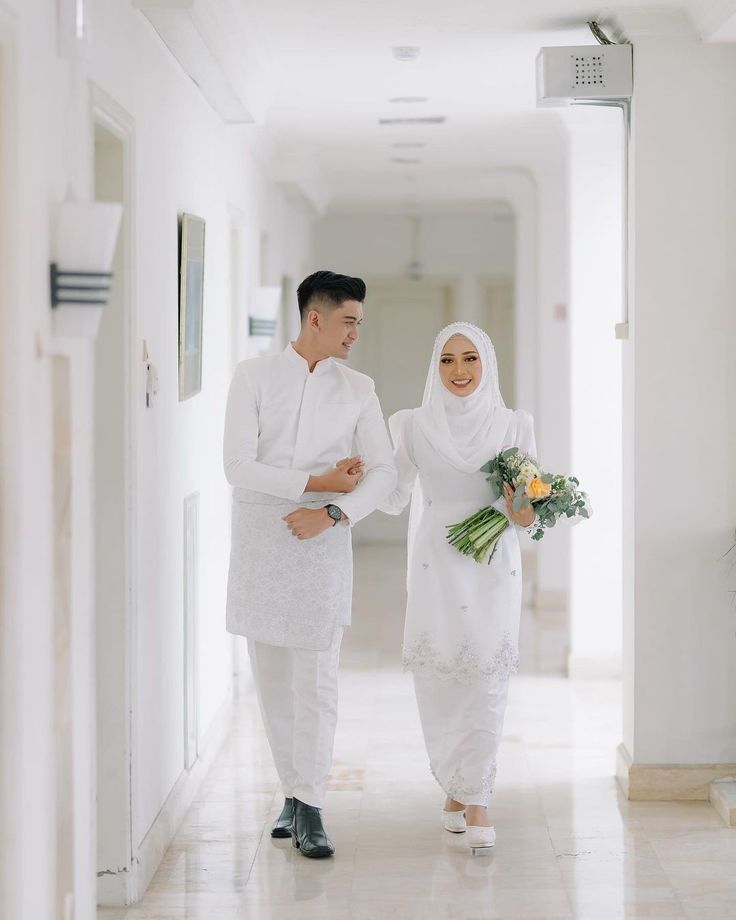 a man and woman are walking down the hall holding flowers in their hands while dressed in white