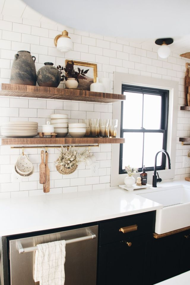 a kitchen with black cabinets and white subway backsplash, open shelving above the sink