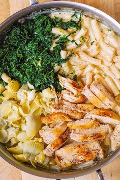 a pan filled with pasta, chicken and spinach on top of a wooden table