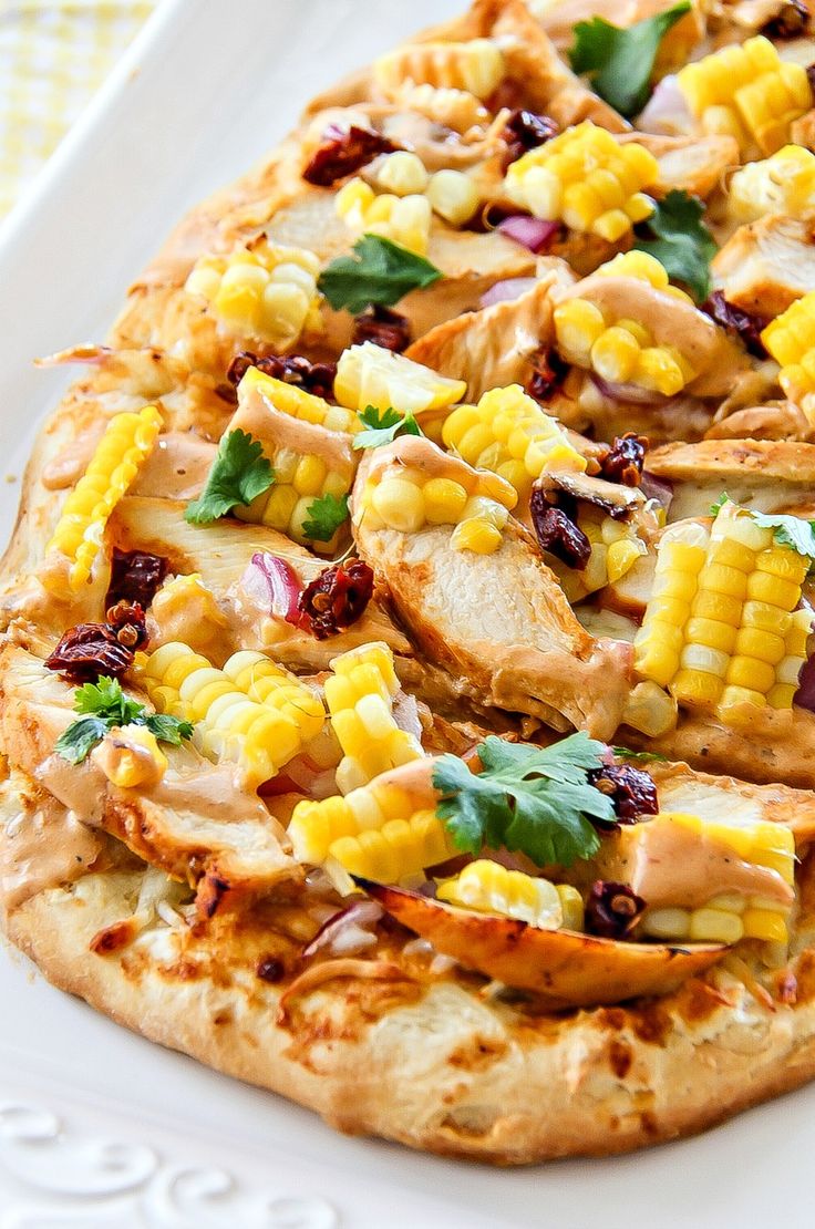 a pizza topped with chicken, corn and cilantro on top of a white plate