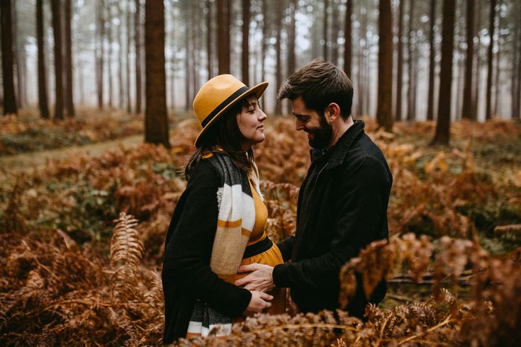 a man and woman are standing in the woods looking into each other's eyes