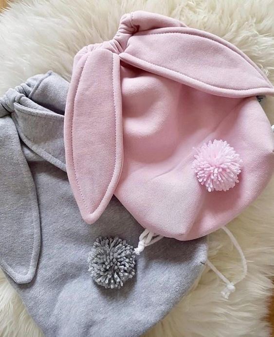 a pink and grey hat with pom - poms on it sitting on top of a fluffy white rug