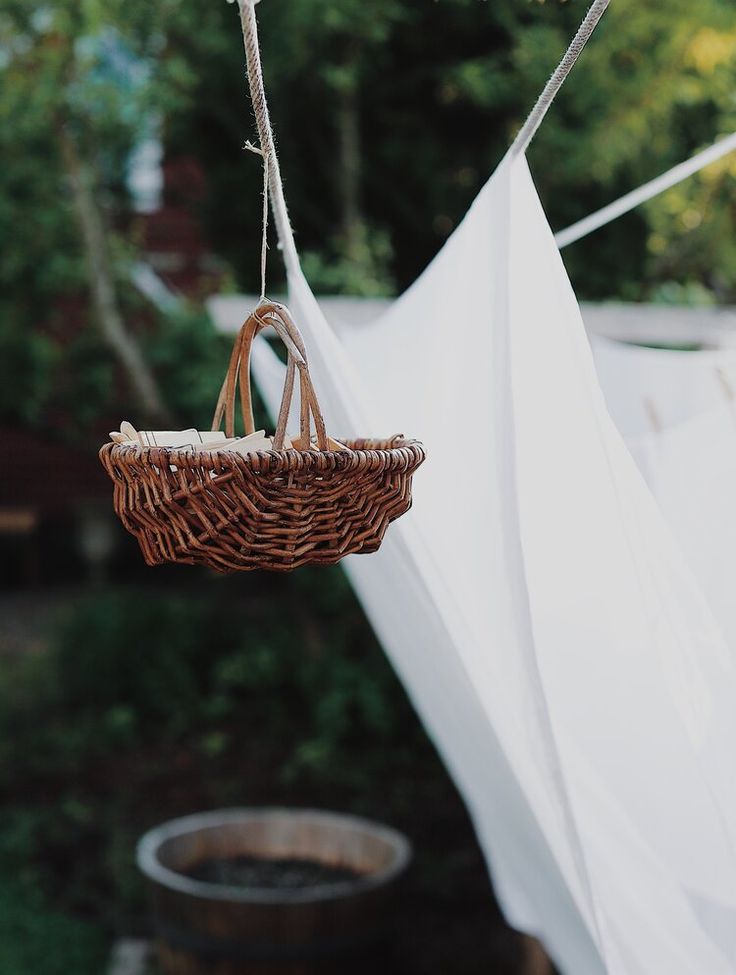 a wicker basket hanging from a clothesline in front of a white tarp