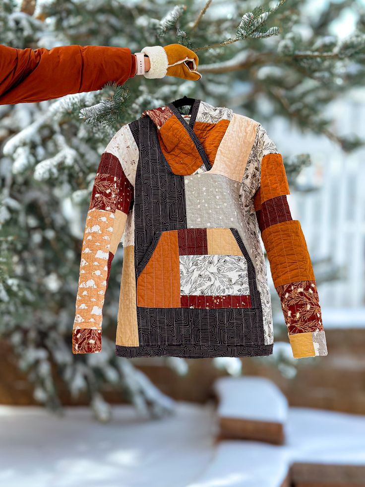 an orange and black jacket hanging from a tree with snow on the ground behind it