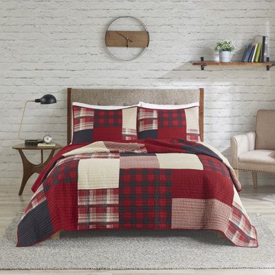 a red and black plaid quilted bed in a room with white brick wall behind it