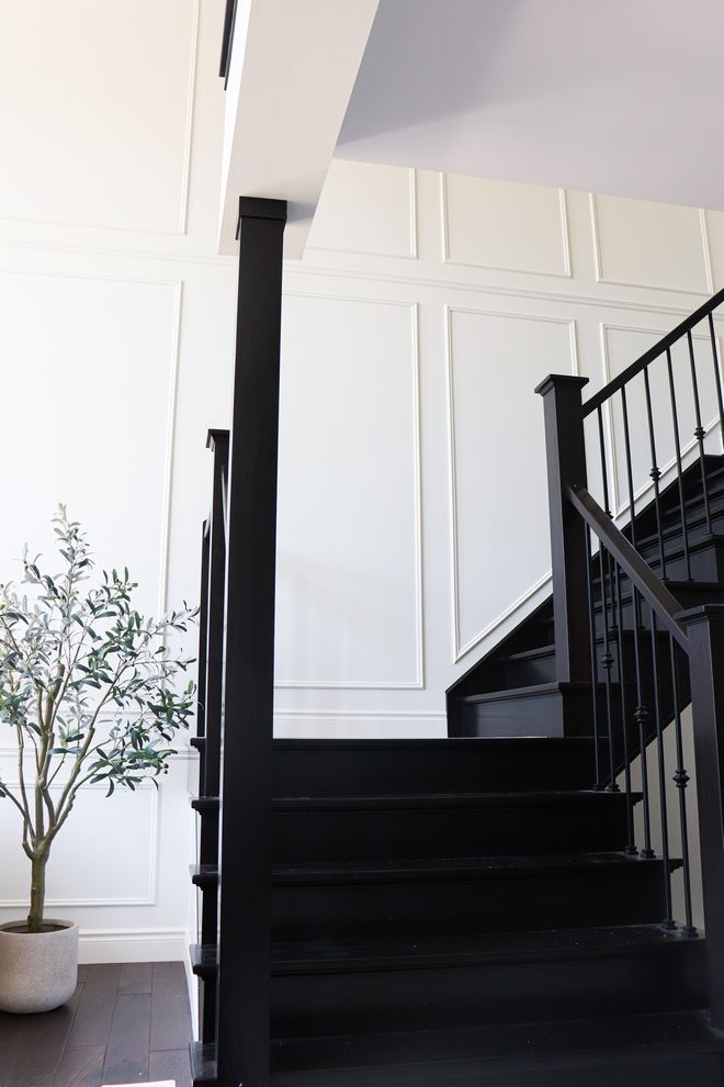 a black stair case next to a tree in a room with white walls and wood floors