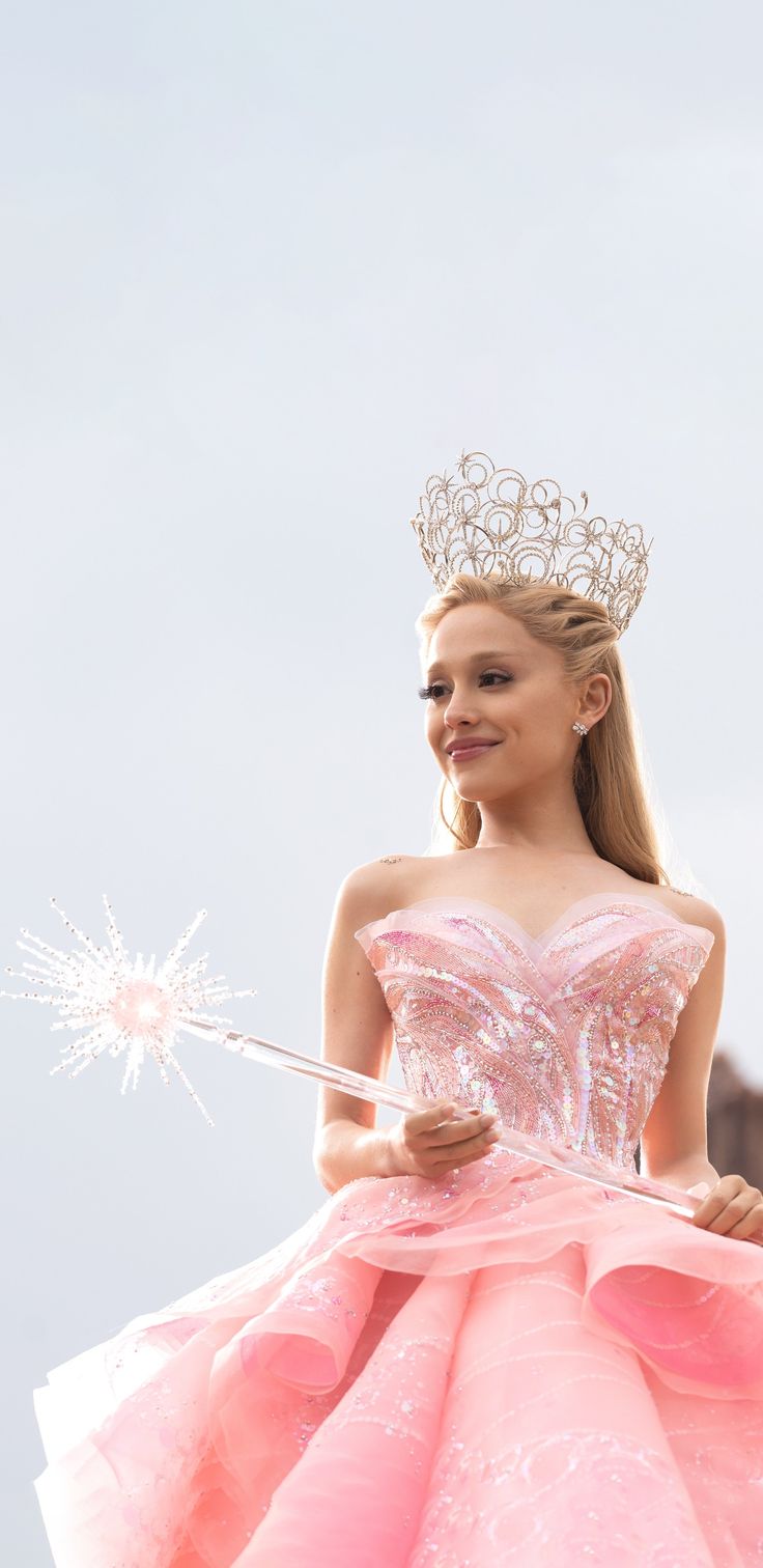 a woman in a pink dress and tiara holding a sparkle wand with her right hand