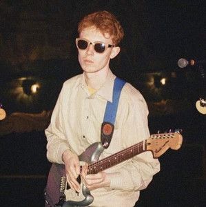 a young man wearing sunglasses and holding an electric guitar in his right hand while standing on stage