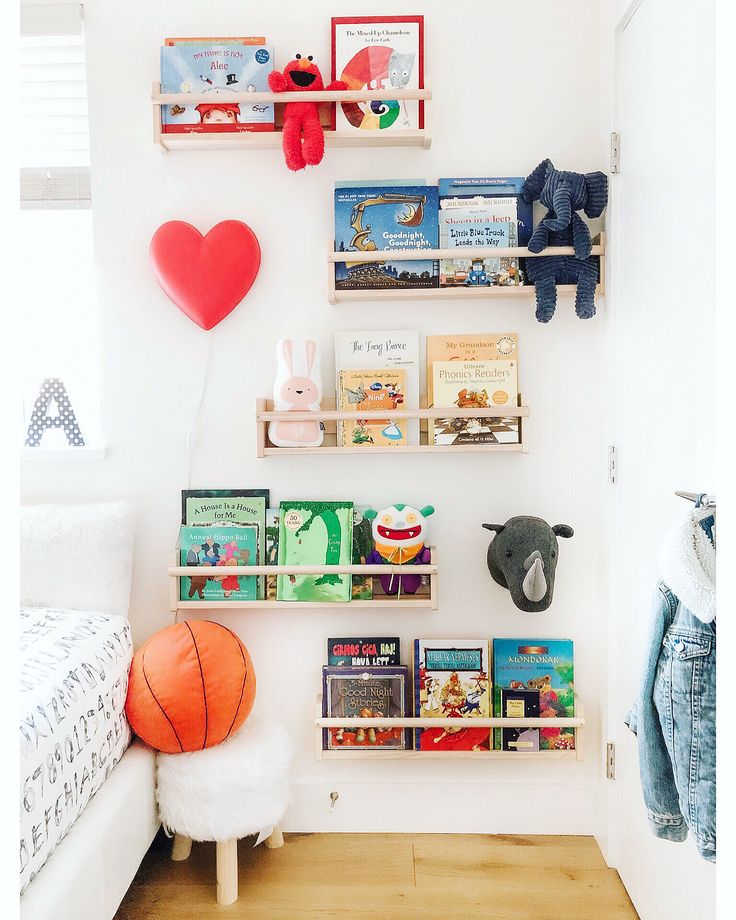 a room with bookshelves, stuffed animals and toys on the wall next to a bed