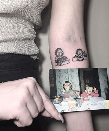 a woman with a small tattoo on her arm holding up a photo and looking at the camera