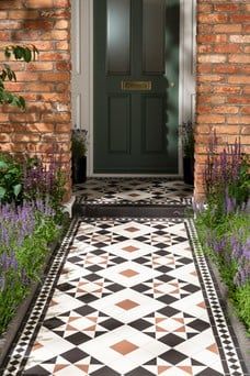 a black and white tiled walkway leading to a front door with purple flowers in the foreground