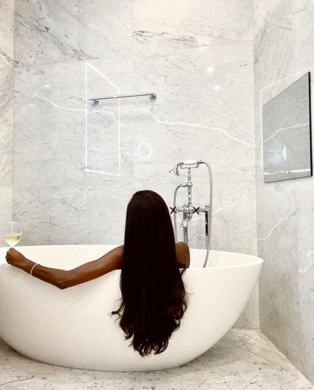 a woman sitting in a bathtub with her long hair hanging over the edge, holding a glass of wine