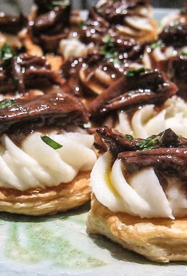 small pastries with meat and cheese on them sitting on top of a tablecloth