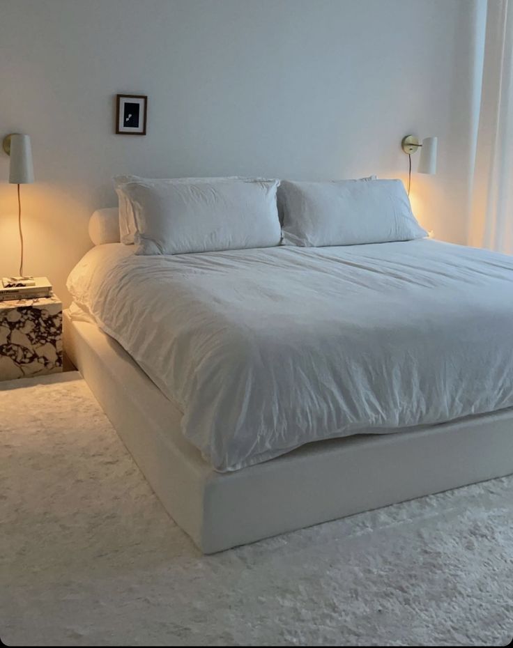 a large white bed sitting in a bedroom next to two lamps on either side of the bed