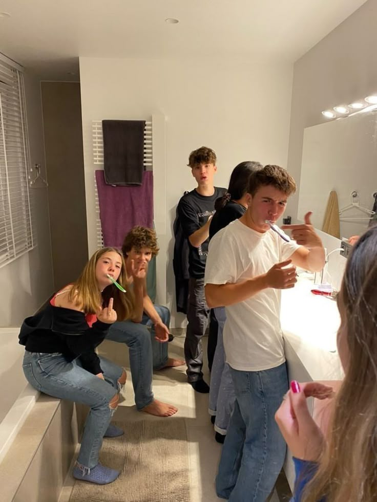 a group of people standing in a bathroom next to each other and brushing their teeth