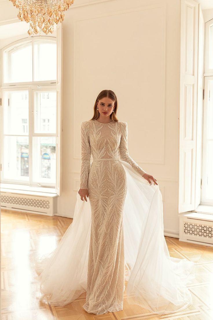 a woman in a long sleeved dress standing on a wooden floor next to a chandelier