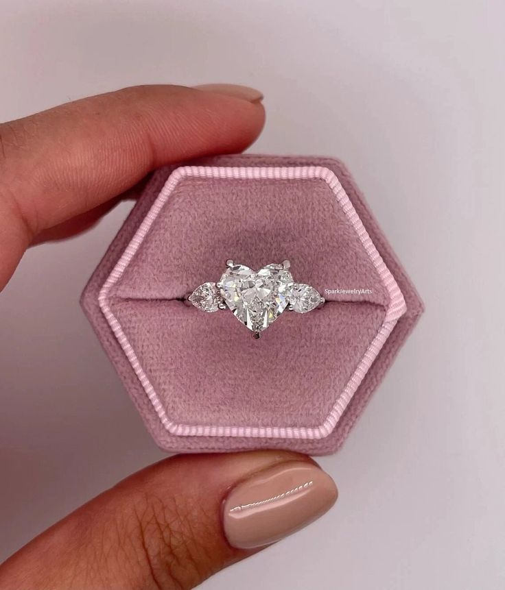 a woman's hand holding an engagement ring in a pink velvet box with two diamonds on it