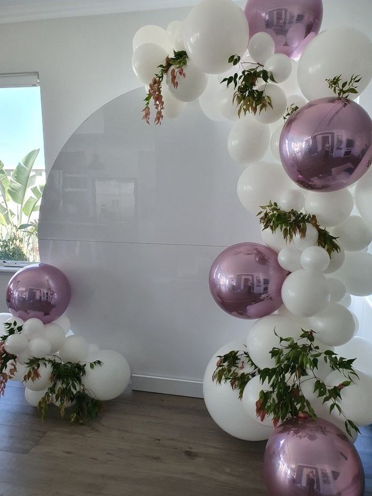 balloons and greenery are hanging from the ceiling in front of a white wall with an arch