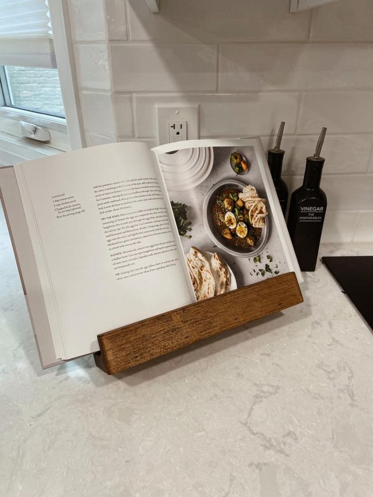 an open book sitting on top of a kitchen counter next to a knife and fork