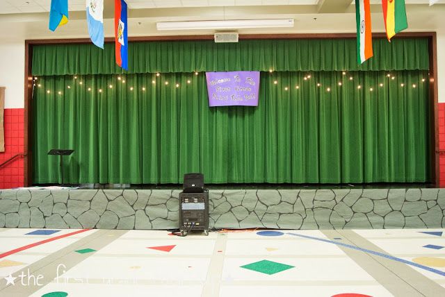 an empty stage with green curtains and colorful flags hanging from it's ceiling in the middle of a room