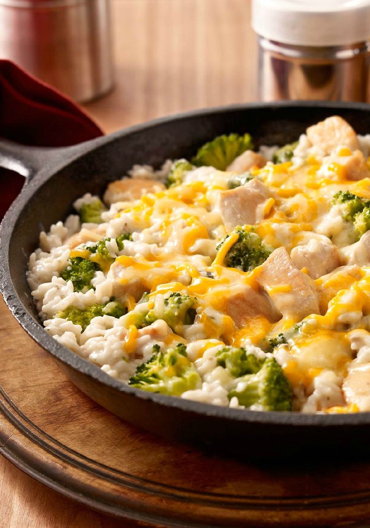 a skillet filled with rice and broccoli on top of a wooden table