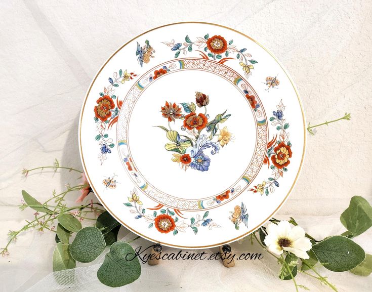 a plate with flowers on it sitting next to some green leaves and white wallpaper