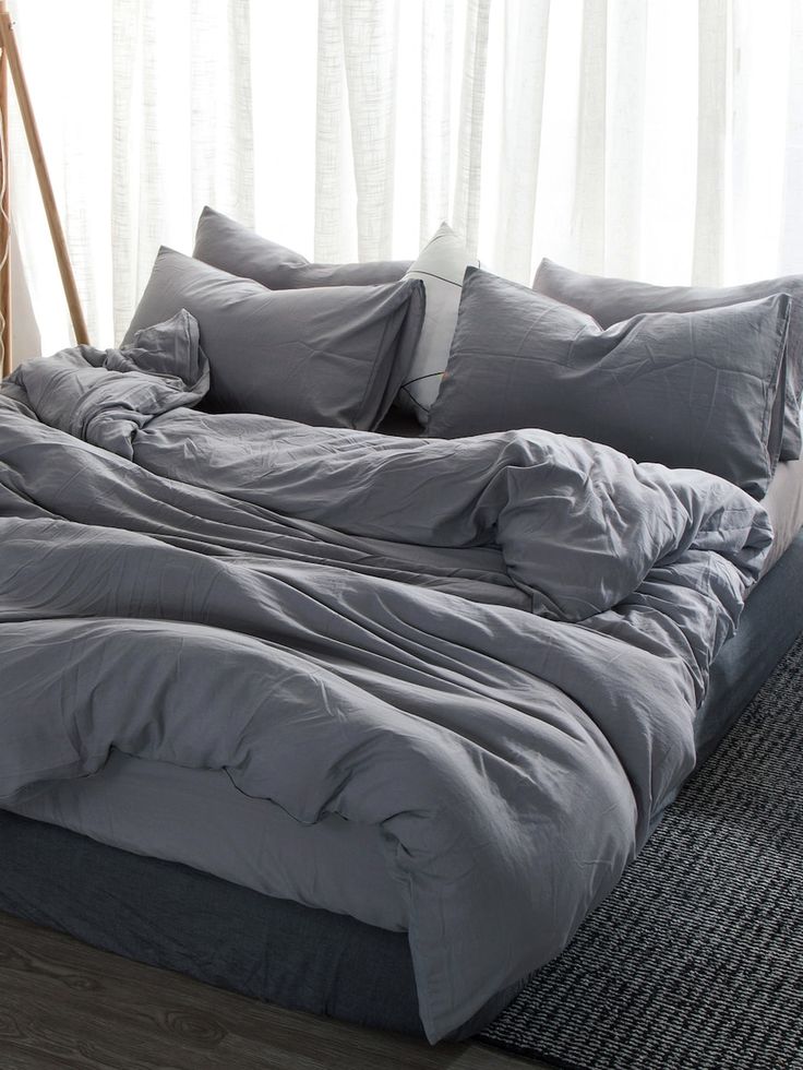 an unmade bed with grey sheets and pillows