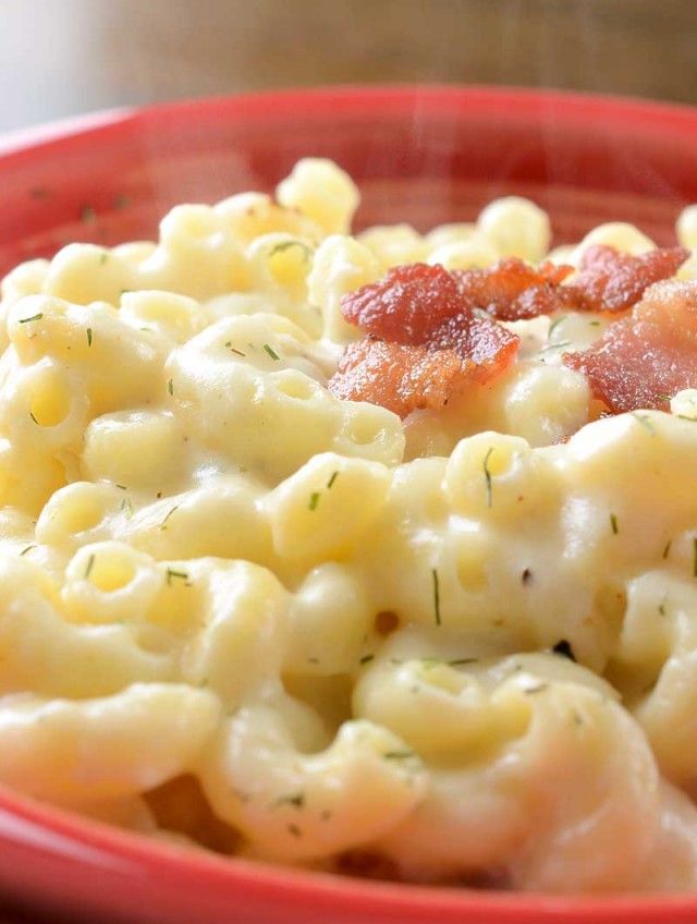 a red bowl filled with macaroni and cheese covered in bacon