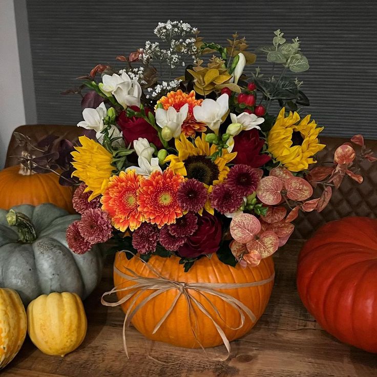 a vase filled with lots of flowers sitting on top of a table next to pumpkins