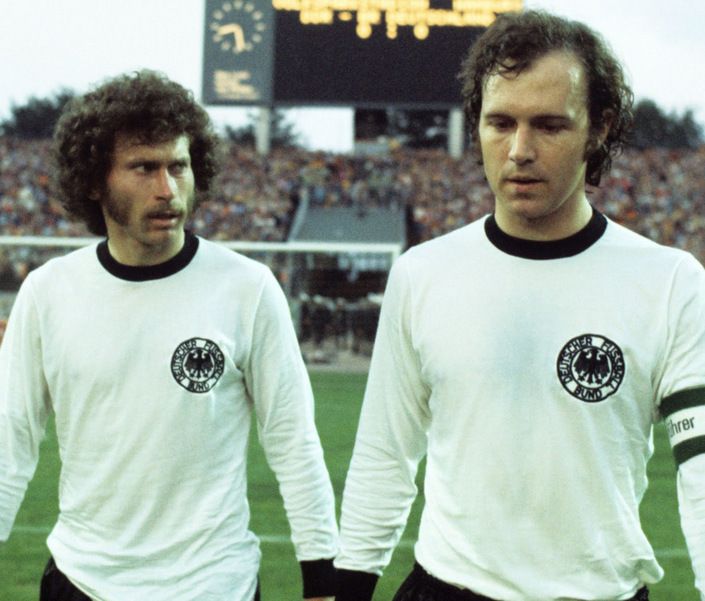 two men standing next to each other in front of a soccer stadium filled with people