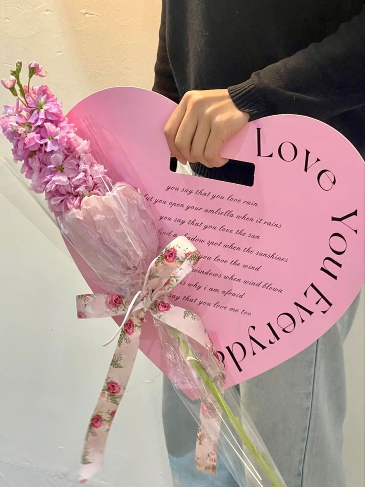 a person holding a pink heart shaped sign with flowers