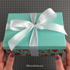 a person holding a wrapped gift box with white ribbon