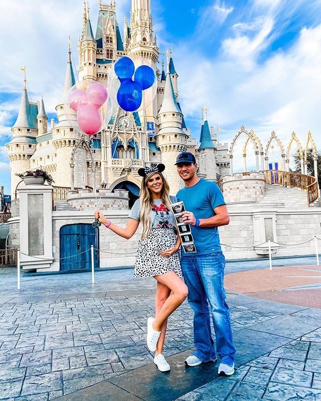 a man and woman pose in front of the castle at disneyland world with balloons flying above them