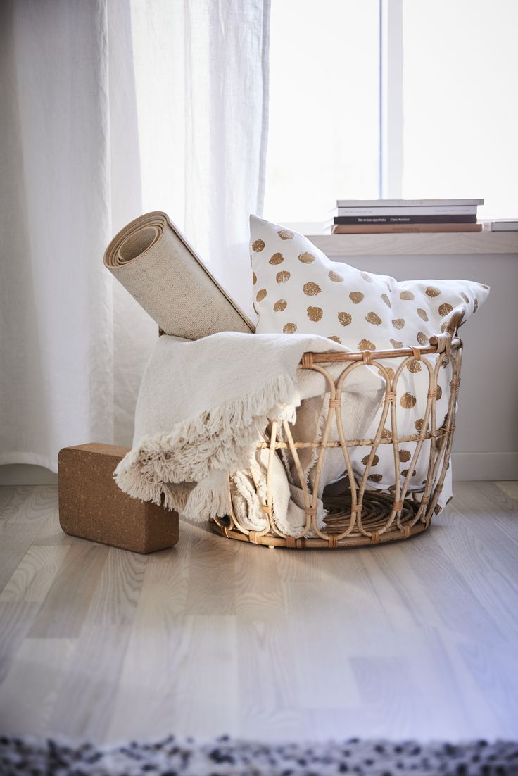 a basket that is sitting on the floor next to some pillows and a pillow in front of a window