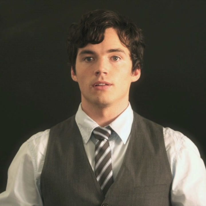 a man wearing a vest and tie standing in front of a black background