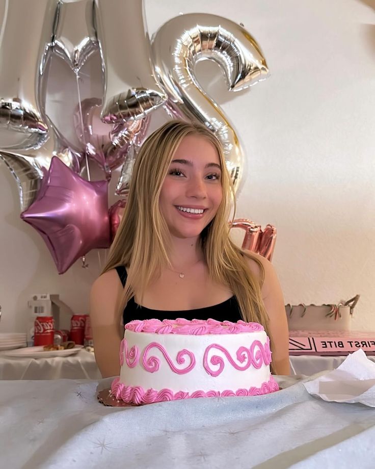 a woman sitting in front of a pink and white cake