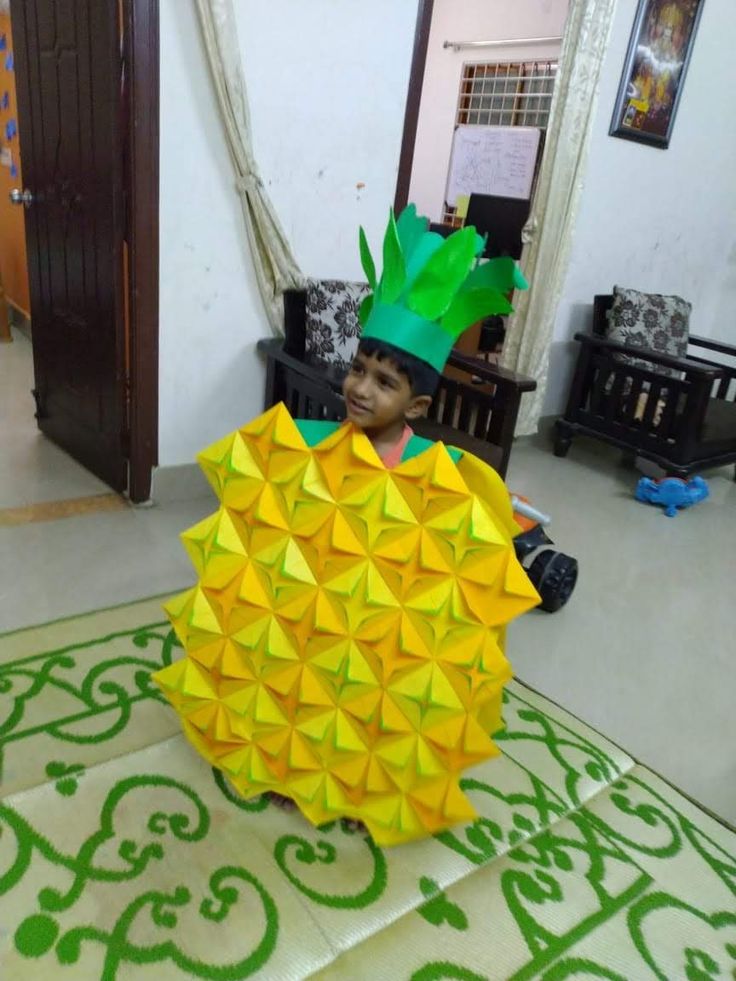 a child in a pineapple costume sitting on the floor with an origami pineapple