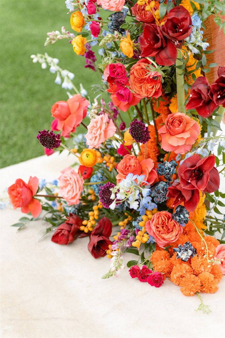 an arrangement of colorful flowers on a table in the grass at a wedding or event