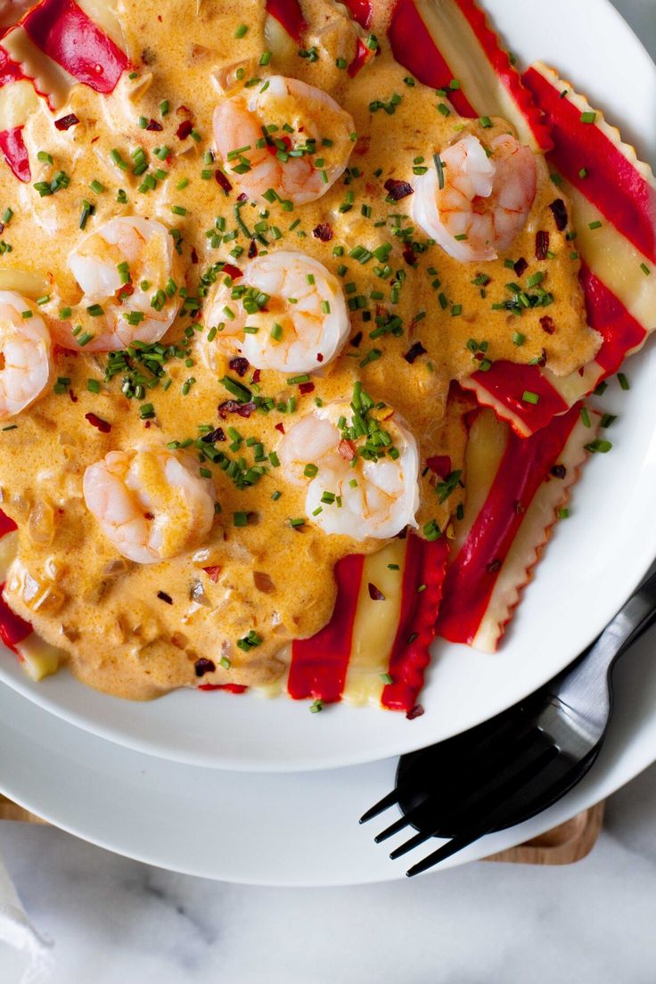 a white plate topped with pasta covered in shrimp and sauce next to utensils