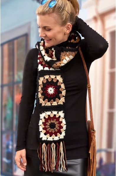 a woman wearing a black top and scarf with crocheted designs on it, standing in front of a building