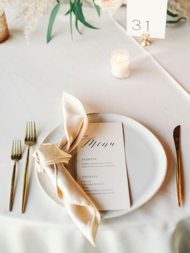 a white plate topped with a menu next to two gold forks and a small candle