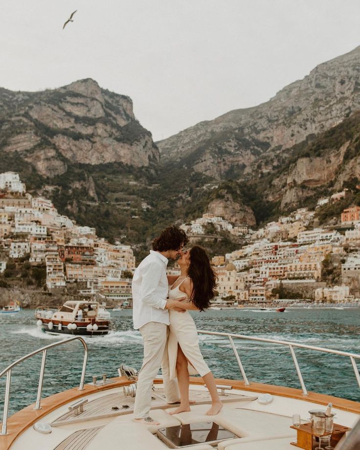 a man and woman kissing on the back of a boat in front of some mountains