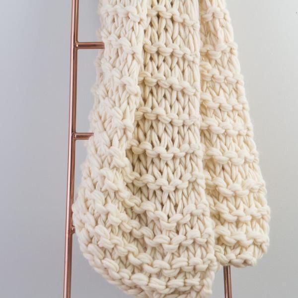 a white knitted scarf hanging from a copper rack