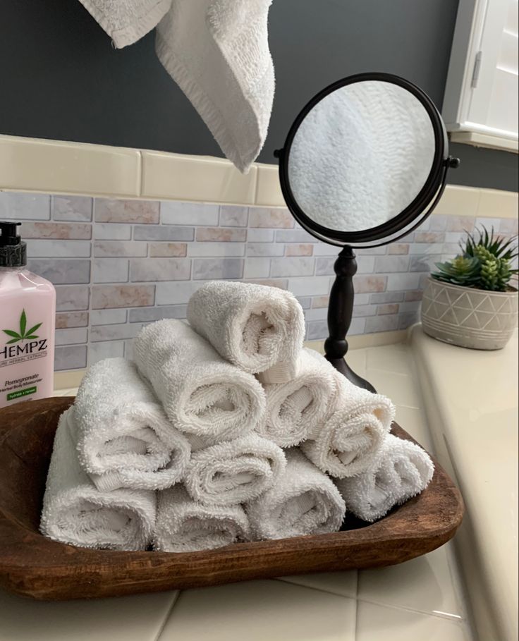 towels are stacked on a wooden tray in front of a mirror with a potted plant next to it